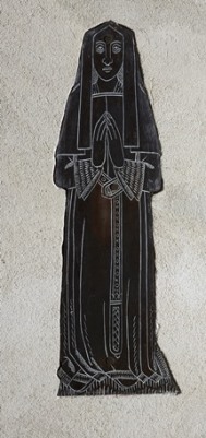 Simply rendered but elegant brass showing a robed woman standing with hands clasped in prayer
